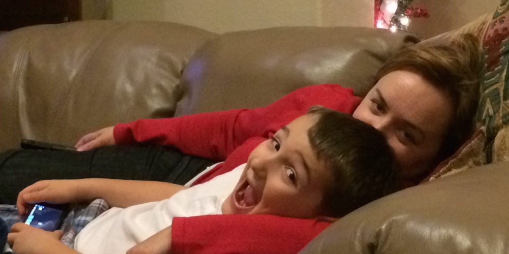 Kid excitedly playing a game on his iPhone while laying on the couch with mom.