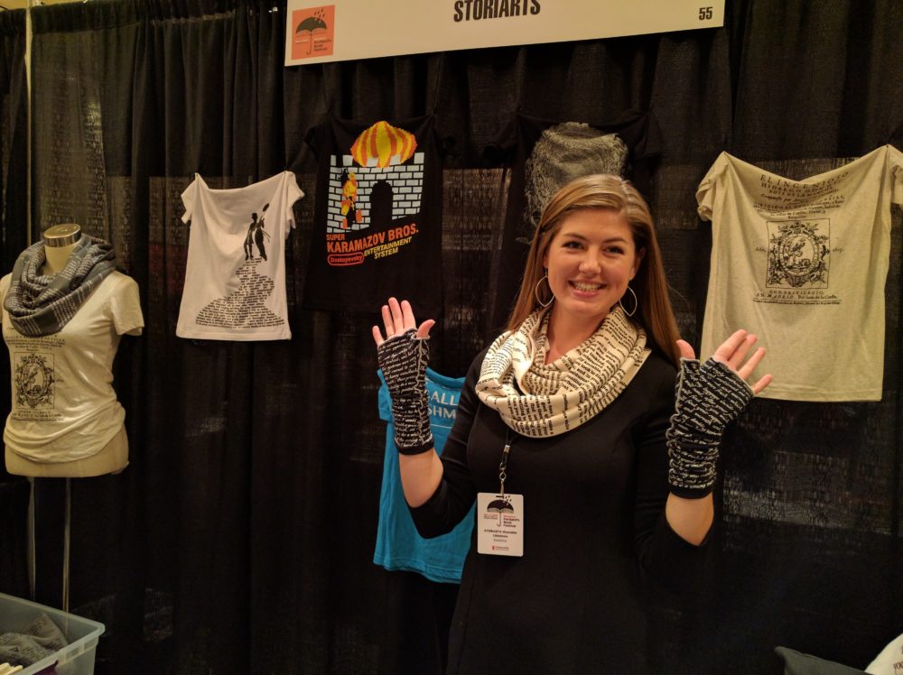 A woman demonstrates her literary scarves and hand warmers