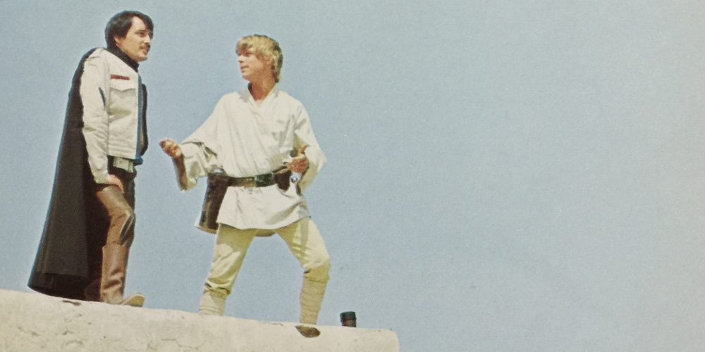 Luke Skywalker stands on the edge of a terrace, talking with his friend Biggs.