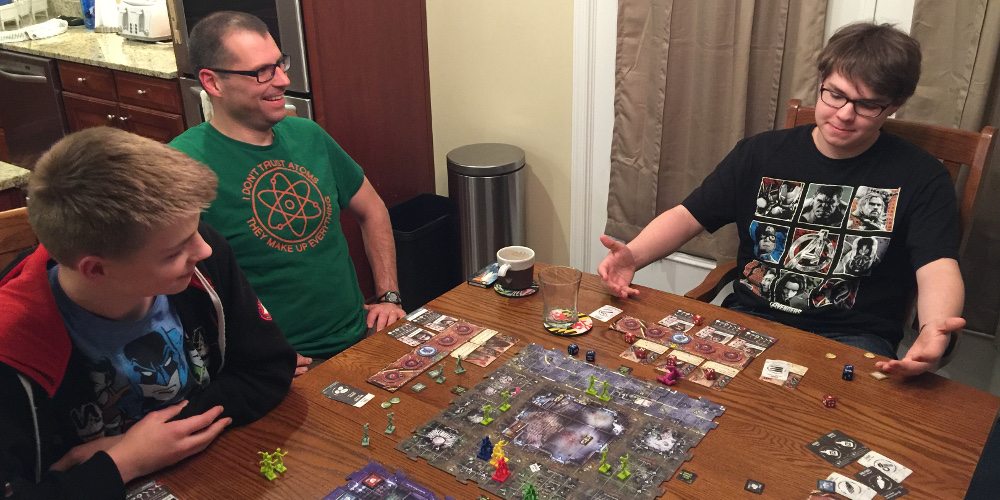 Three people playing Zpocalypse 2; one person has their arms pointed at their survivors and looks quite pleased with how the game has played out.