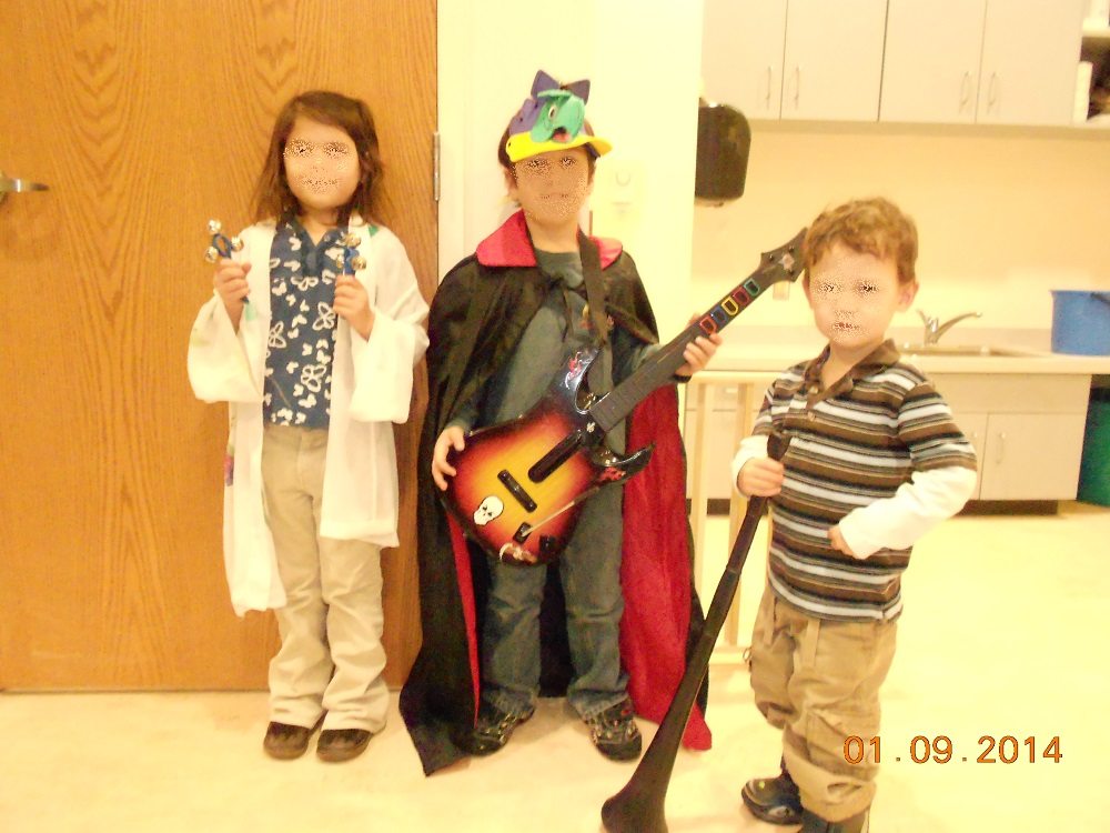 three children in random bits of costume hold toy instruments