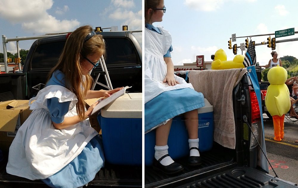 Girl in Alice in Wonderland costume reads in the back of a truck and watches another marcher in a duck costume - first cosplay