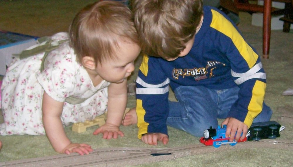 3yo plays with a Thomas the Tank Engine while his 1yo sister looks on closely