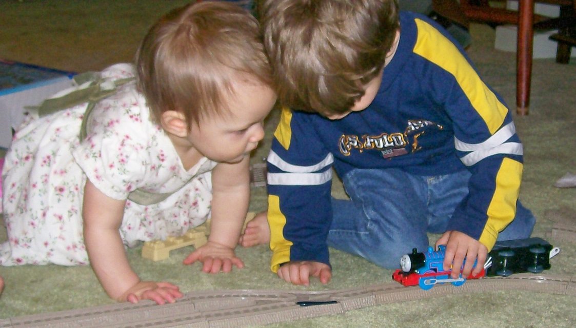 3yo plays with a Thomas the Tank Engine while his 1yo sister looks on closely