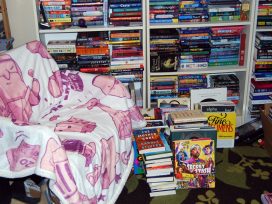 Comfy chair next to full bookshelves and stacks of books on the floor