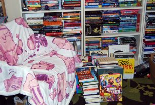 Comfy chair next to full bookshelves and stacks of books on the floor